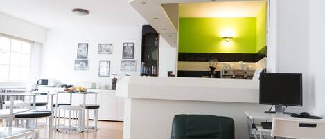 A modern kitchen with a green accent wall, a dining area with bar stools, and a computer desk with a monitor.