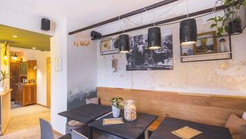 Ein gemütliches Café mit Holztischen und -bänken, Pendelleuchten und einer rustikalen Wand mit gerahmten Bildern.