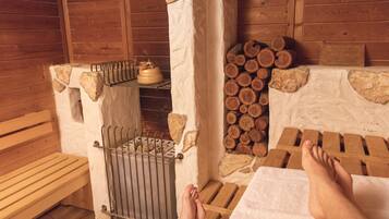 A sauna room with wooden benches, a metal rack, and a stone wall with stacked logs.