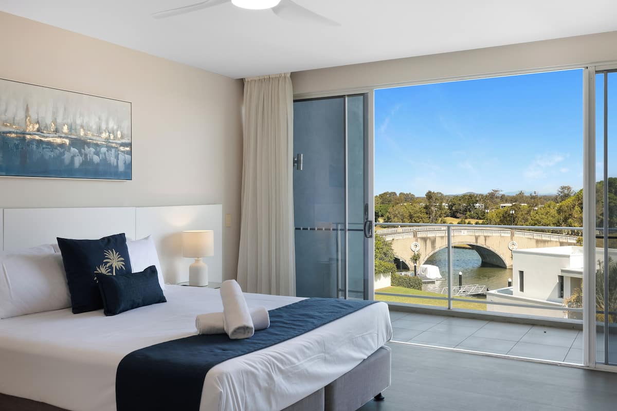 A hotel room with a large bed, a view of a bridge, and a balcony with a glass door.