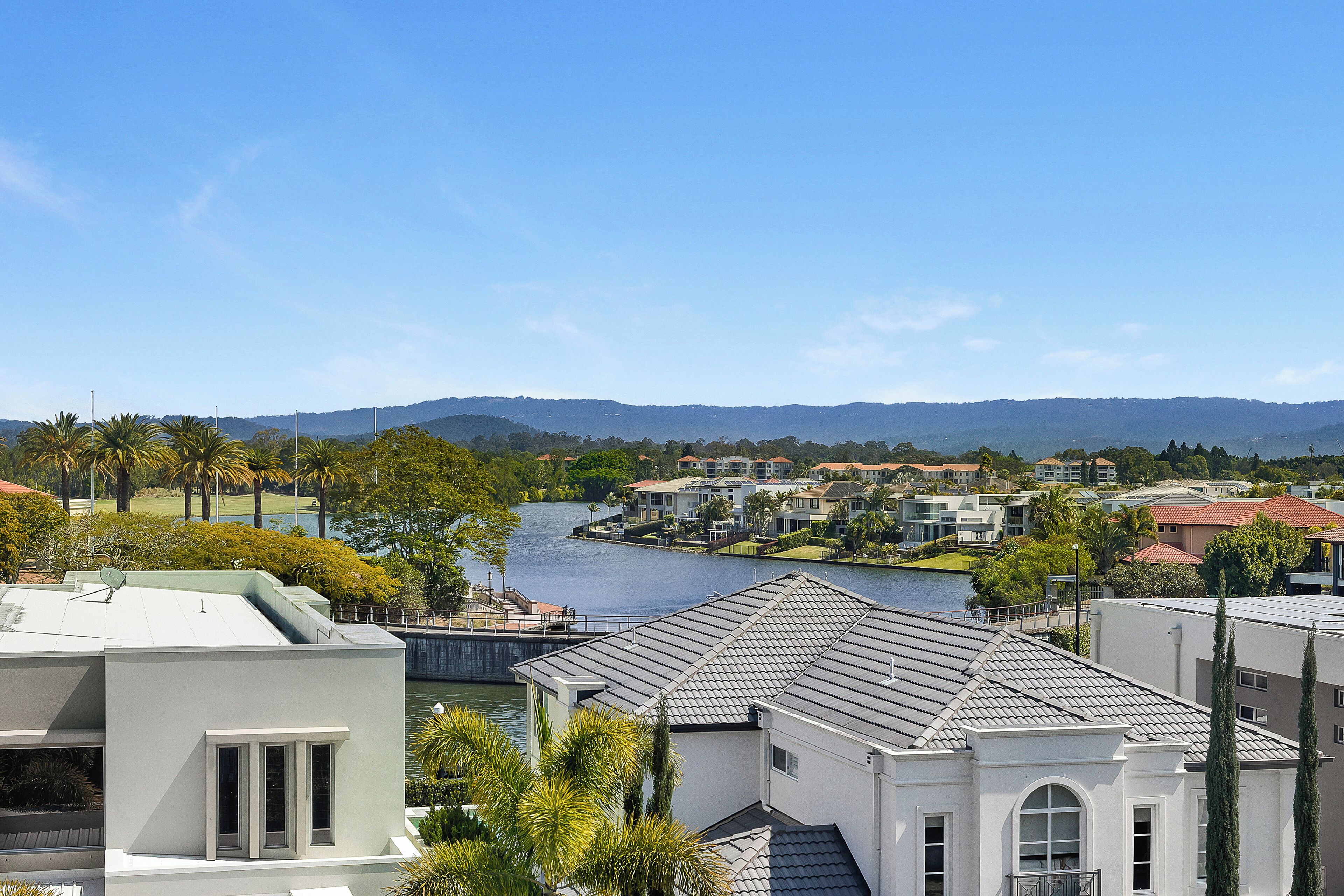A residential area with houses near a body of water, surrounded by greenery and hills.
