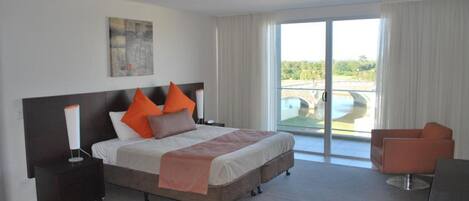 A hotel room with a bed, a nightstand, a chair, and a view of a pool through a sliding glass door.