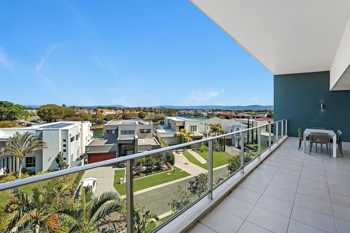 A balcony with a view of modern buildings, a table with chairs, and a railing.