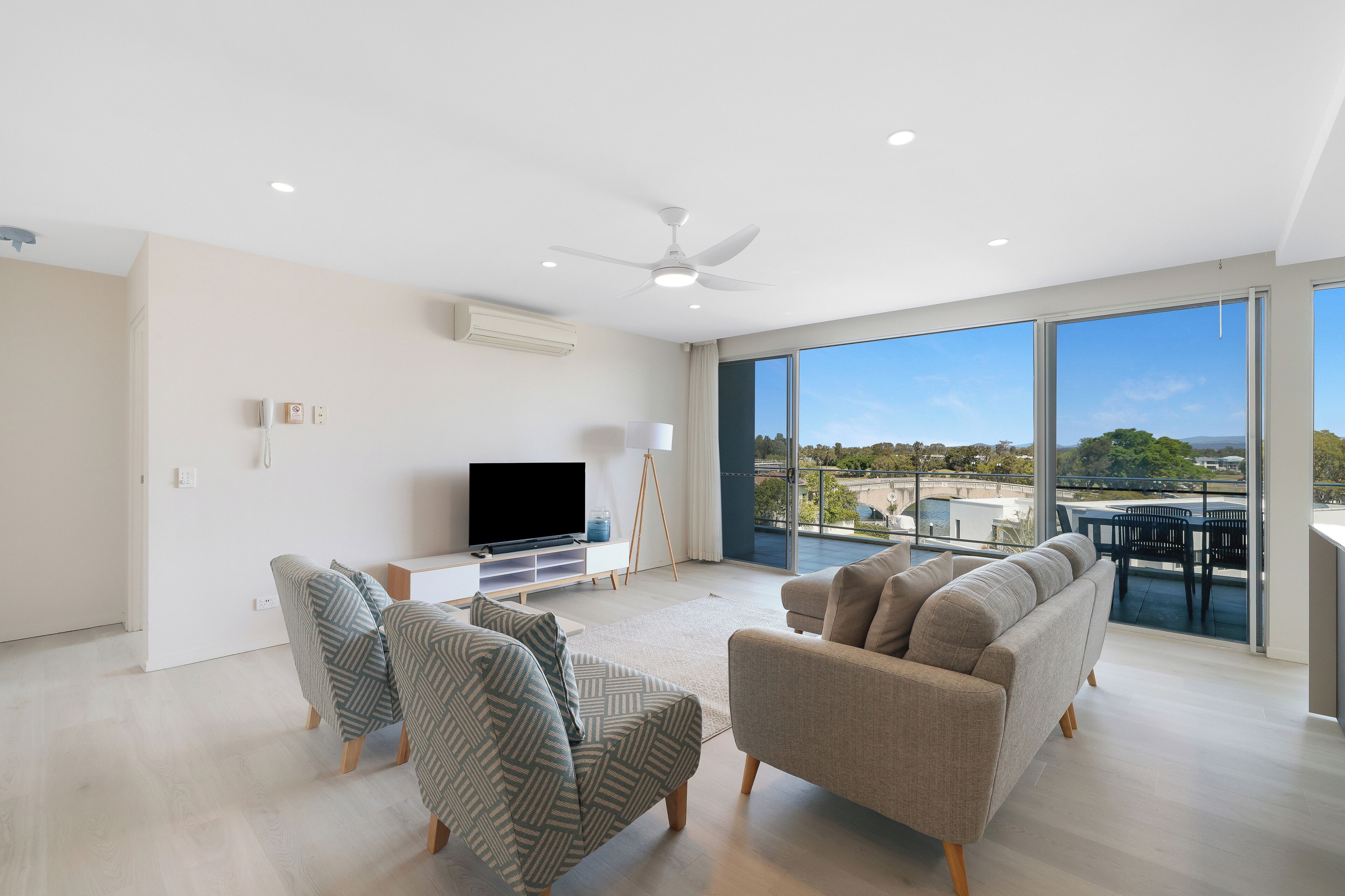 Una sala de estar moderna con sofá, sillones, televisor y un balcón con vistas.