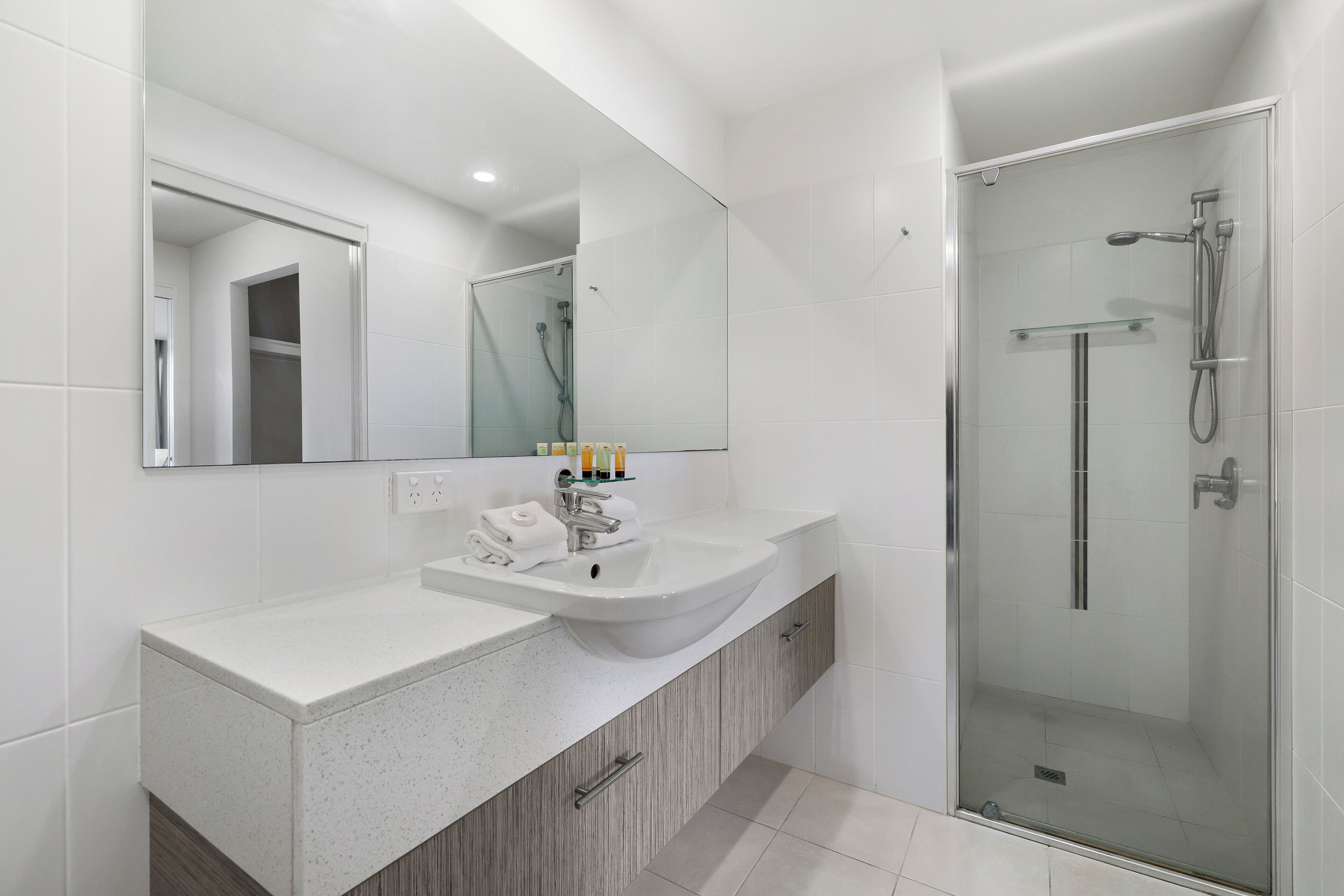 Un baño moderno con lavamanos doble, un espejo grande y una zona de ducha con cerramiento de vidrio.