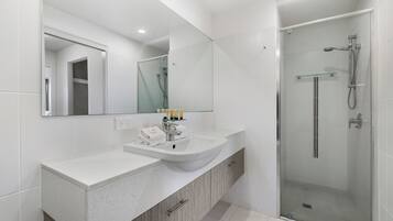 Un baño moderno con lavamanos doble, un espejo grande y una zona de ducha con cerramiento de vidrio.