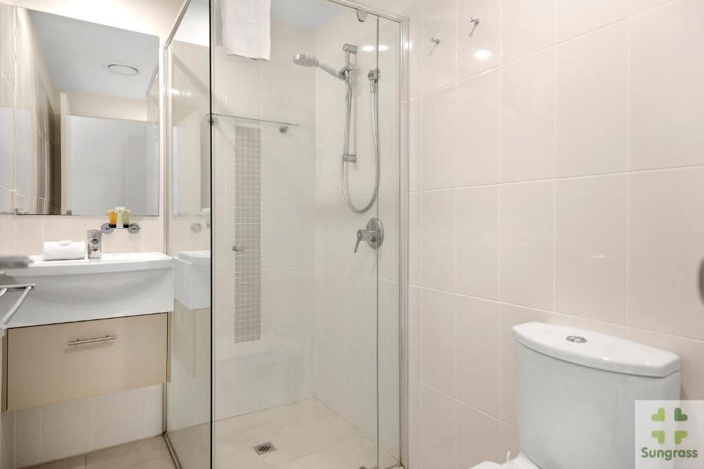 A modern bathroom with a glass-enclosed shower, a white toilet, and a sink with a mirror above it.