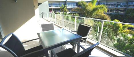 A balcony with a table and chairs, overlooking a building with multiple balconies and greenery.