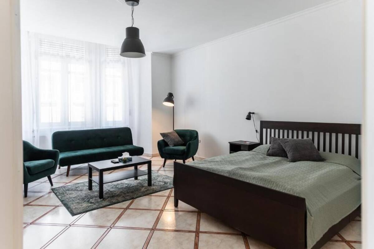 A modern bedroom with a bed, a green sofa, a small table, and two chairs.