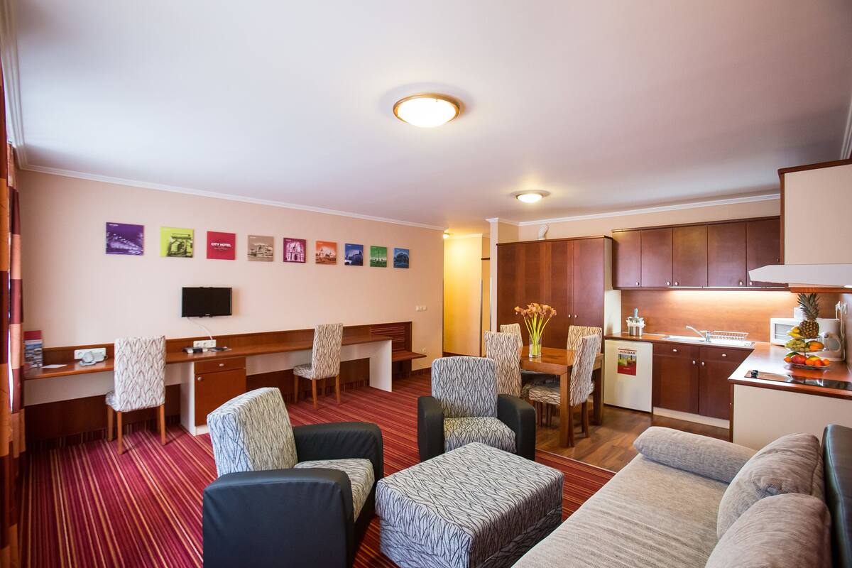 A hotel room with a living area, kitchenette, and a TV mounted on the wall.