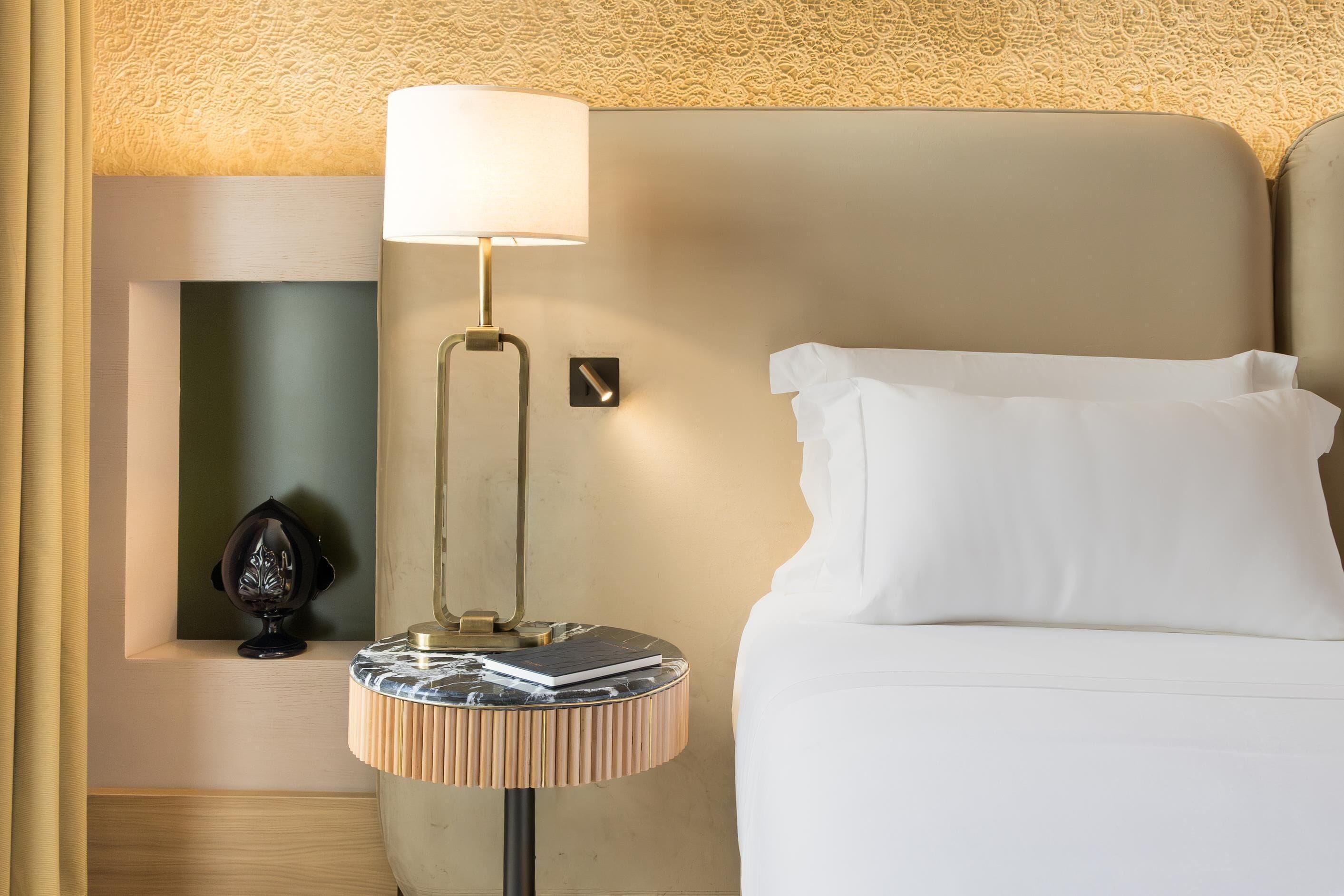A neatly made bed with a white pillow, a bedside lamp, and a small table with a book and a decorative item.