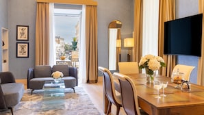 Habitación de hotel con sofá, mesa de comedor, sillas, televisión y vistas de la ciudad.