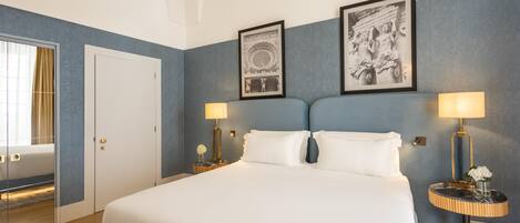 Une chambre d’hôtel avec un grand lit, deux tables de chevet avec des lampes, un tableau encadré au mur et une porte avec un miroir.