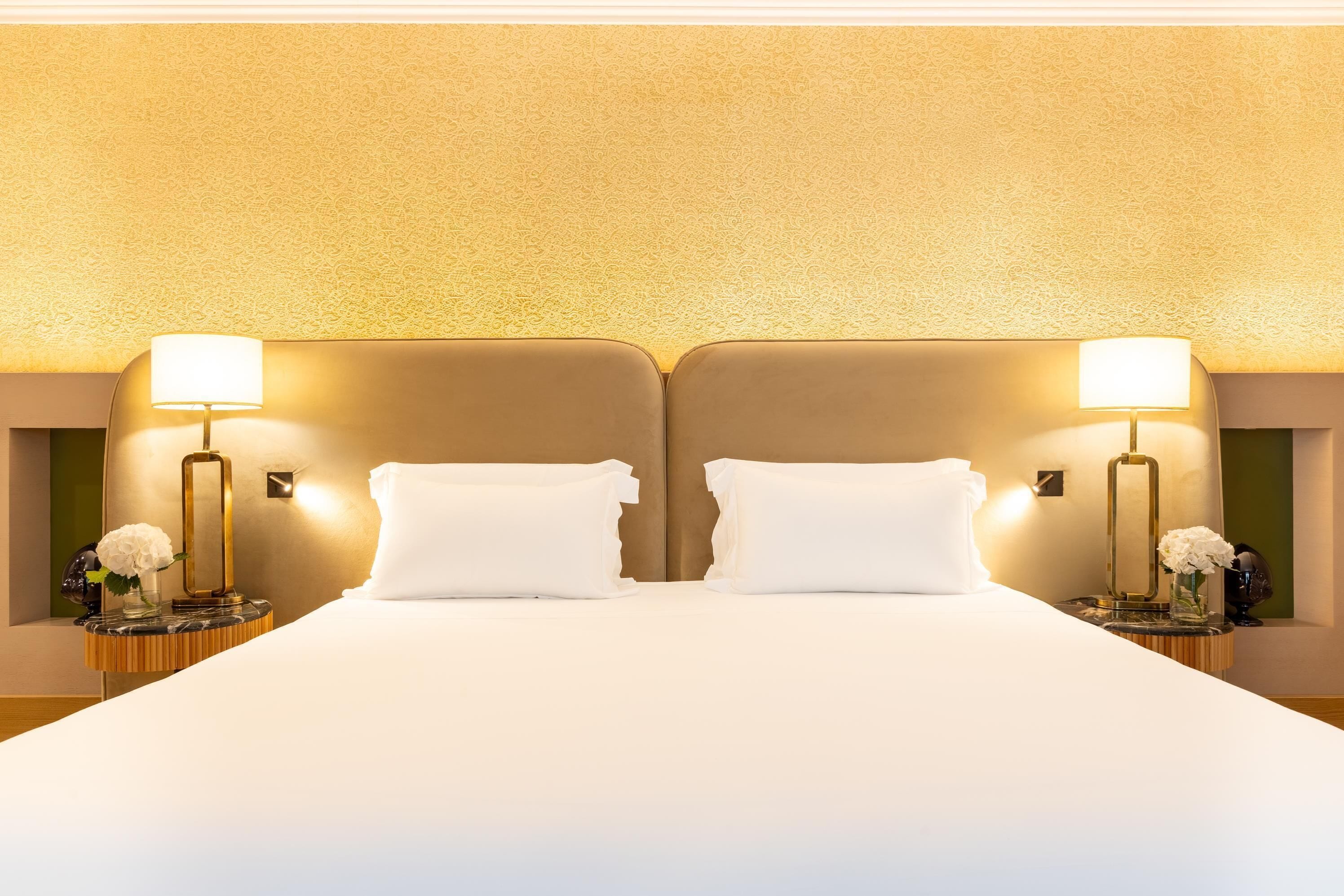 A double bed with two bedside tables, each with a lamp and a vase of flowers.