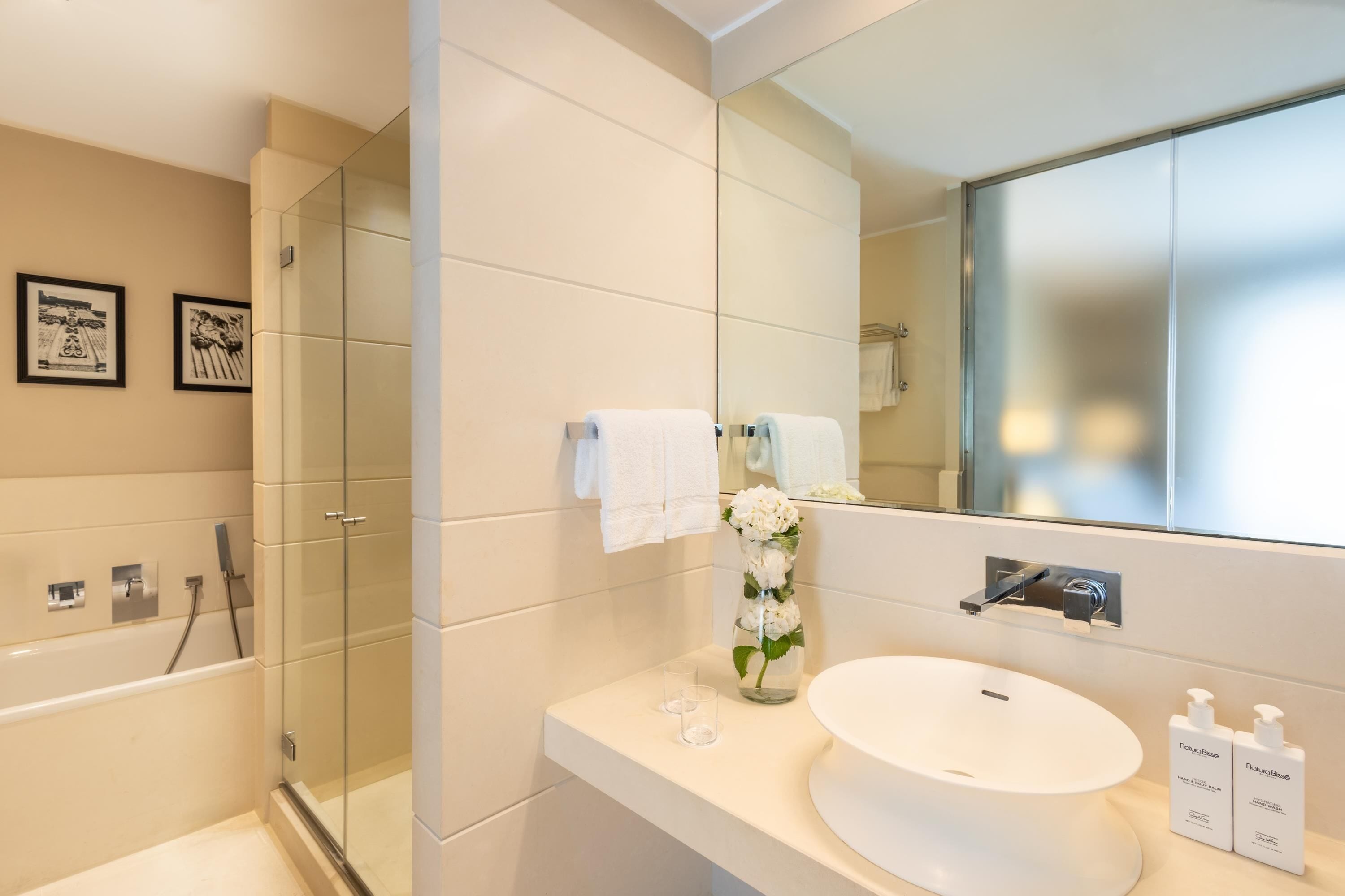 A modern bathroom with a glass shower enclosure, a white sink with a round basin, and two bottles of Dove body wash on the countertop.