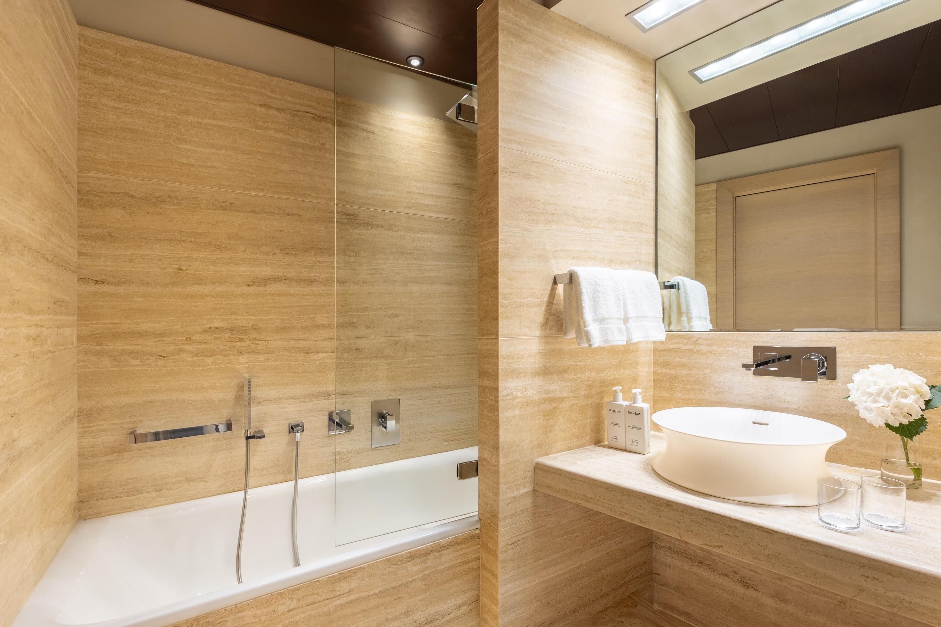 Ein modernes Badezimmer mit einer Badewanne, einem großen Spiegel und einem Waschbecken mit Blumen in einer Vase.