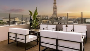 Terraza en la azotea con mobiliario blanco, una planta y vistas a una torre histórica.