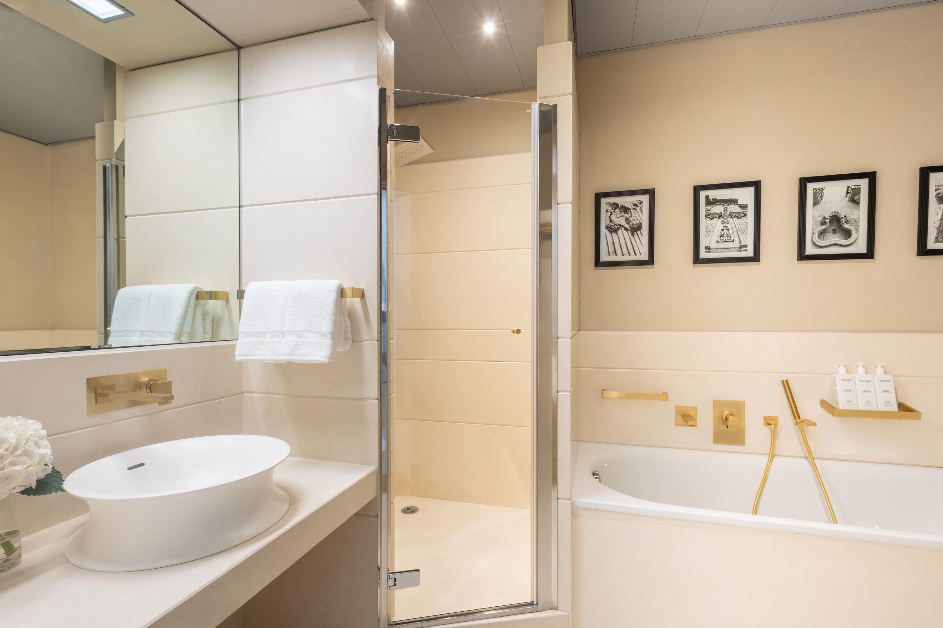 Un baño moderno con un espejo grande, un lavabo redondo, una bañera y cuadros en la pared.