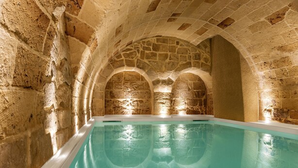Una piscina con arcos de piedra y un muro de piedra.