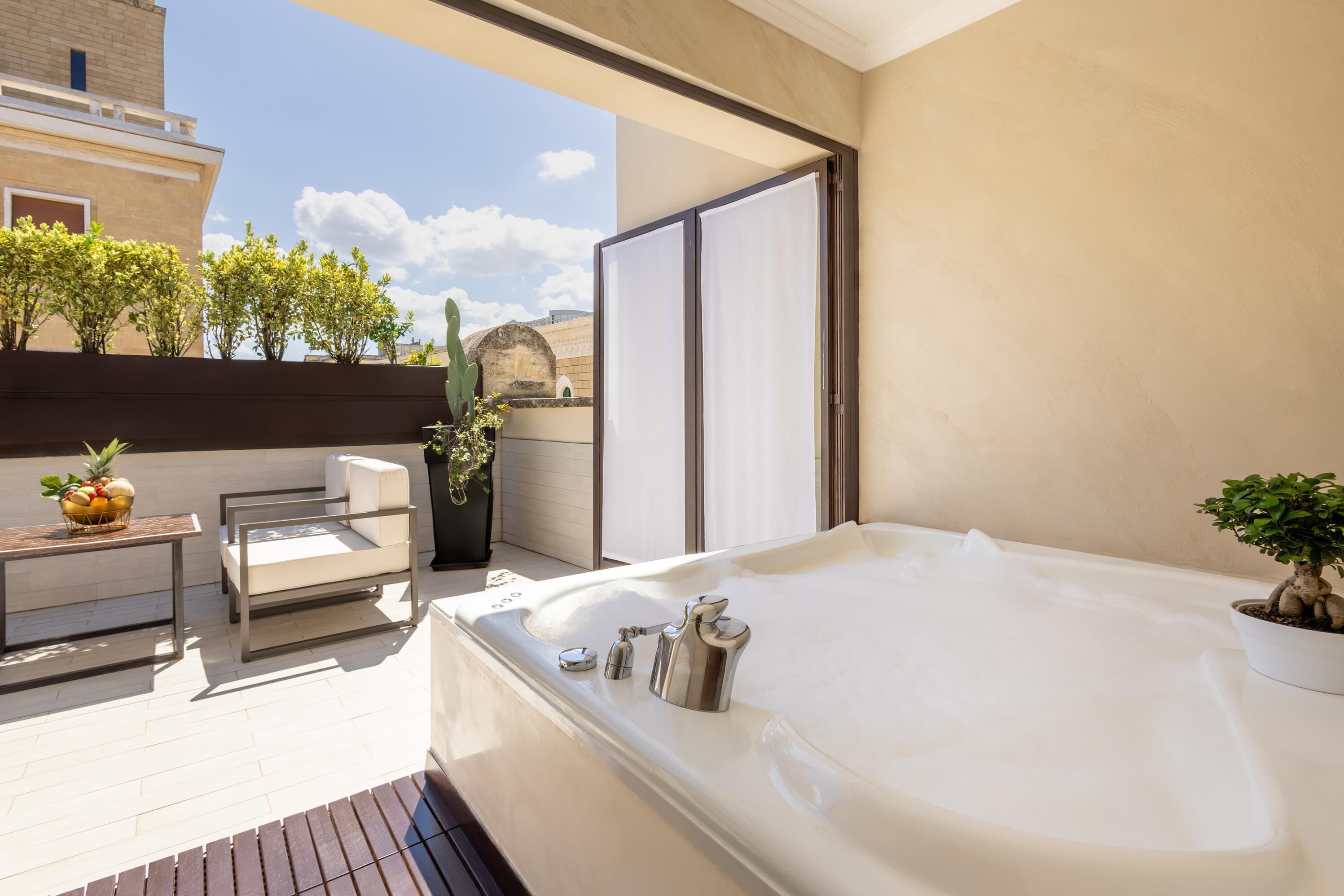 Un balcón con un jacuzzi, una mesa con fruta, una silla y plantas en macetas.