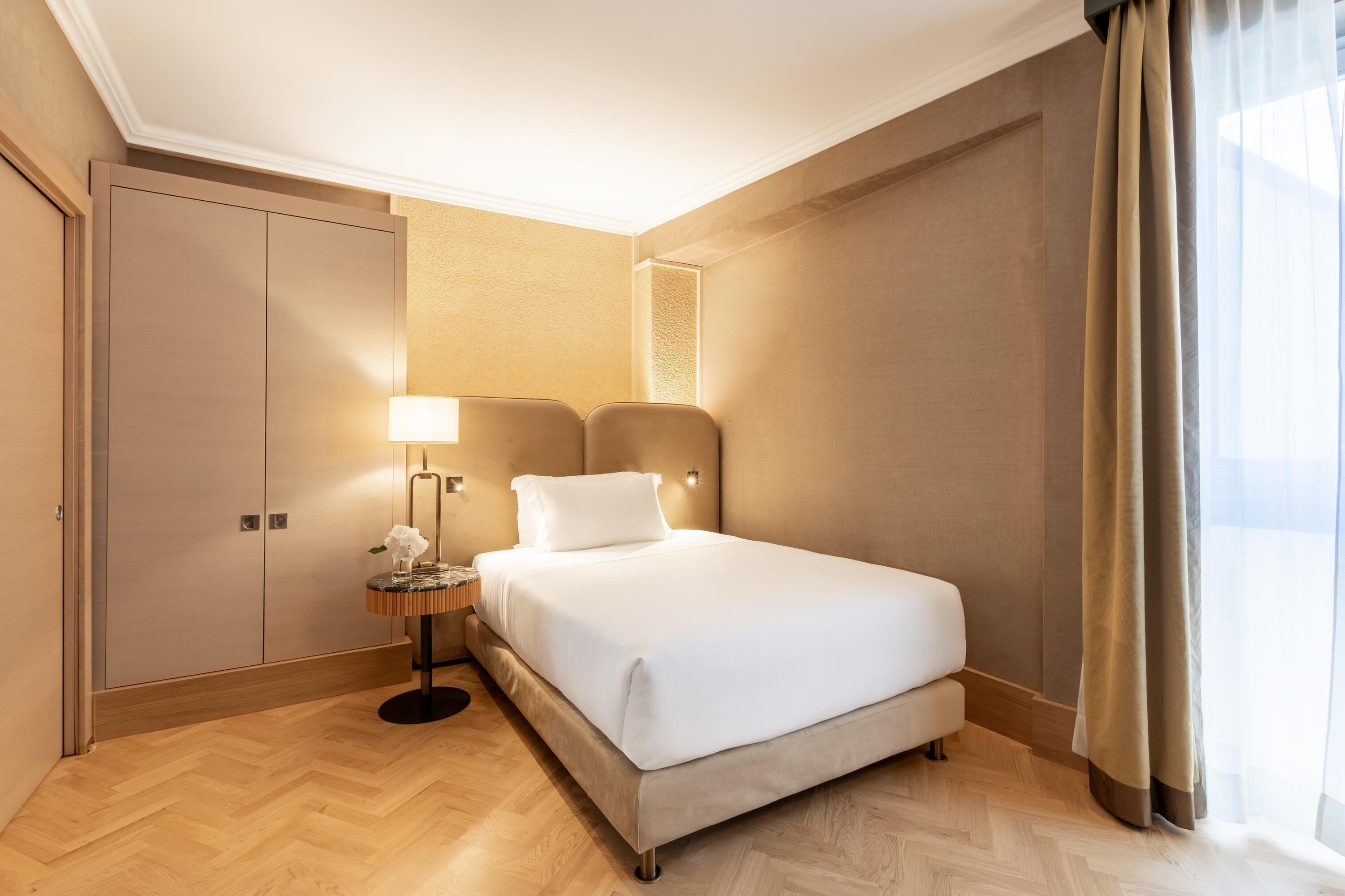 A hotel room with a bed, a nightstand, a lamp, and a wardrobe.