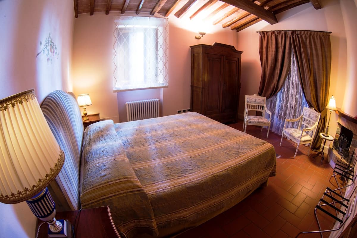A bedroom with a bed, a radiator, a window with curtains, a wardrobe, and a chair.