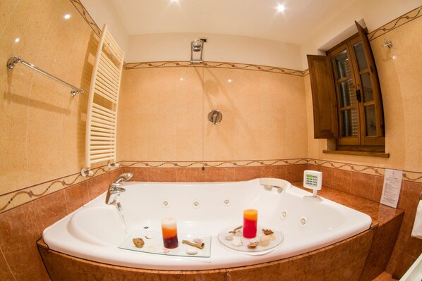 A large, curved bathtub with two candles and seashells, a handheld showerhead, and a wooden cabinet with glass doors.
