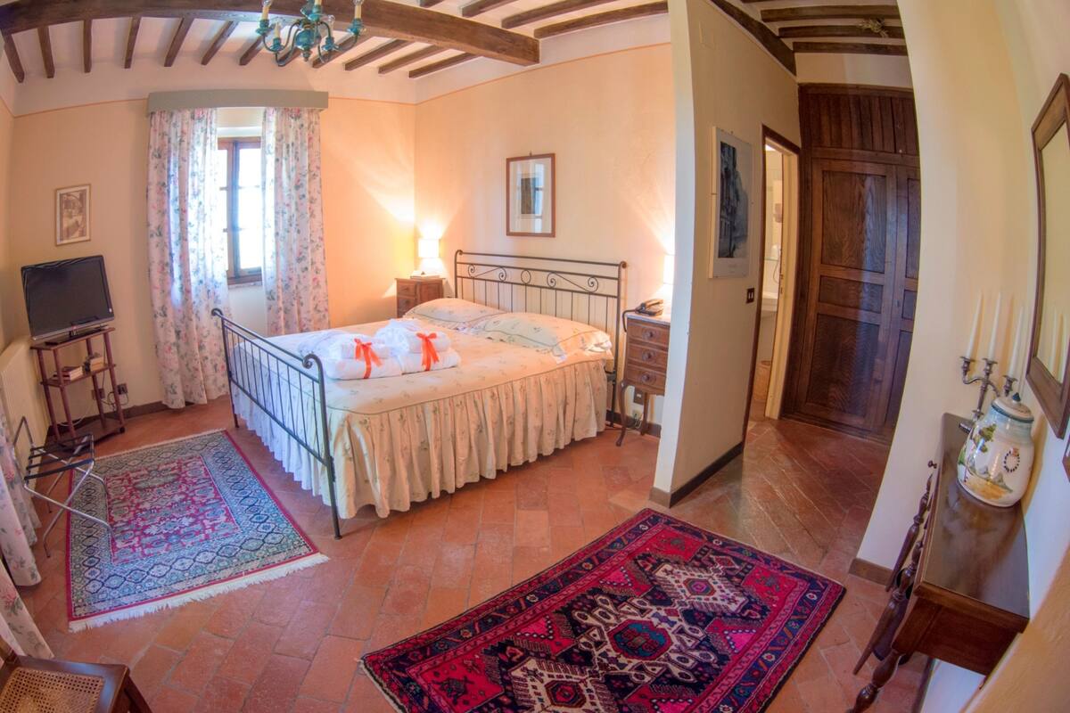 A bedroom with a bed, a TV, a dresser, and a window with curtains.