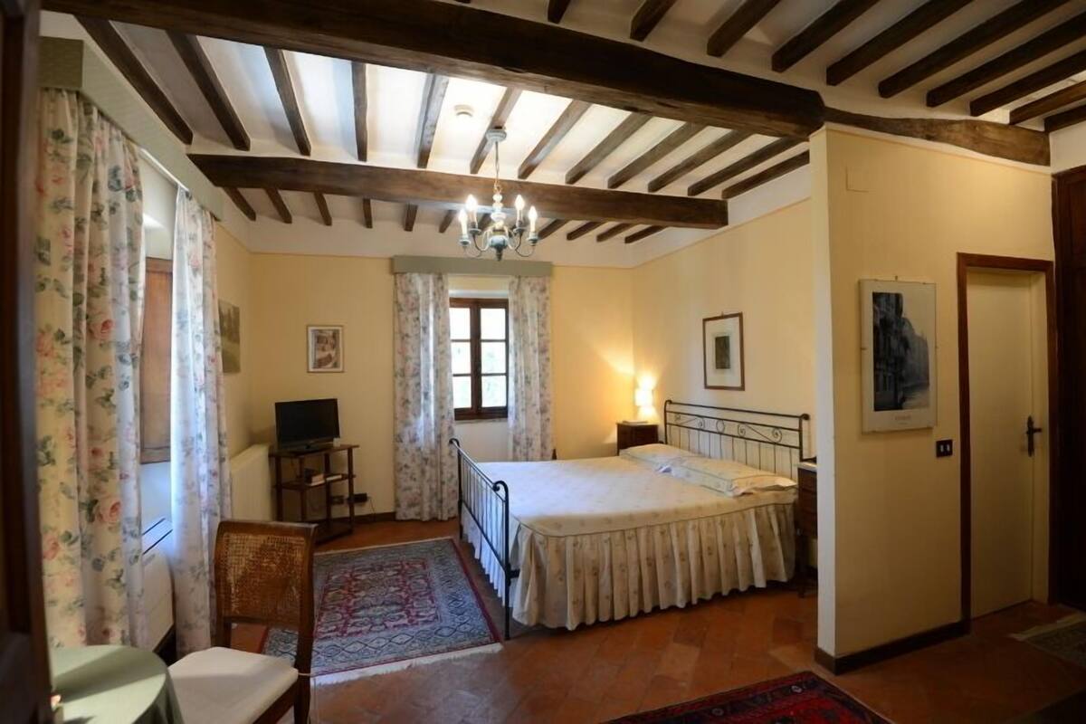 A bedroom with a bed, a desk, a chair, a TV, and a chandelier.