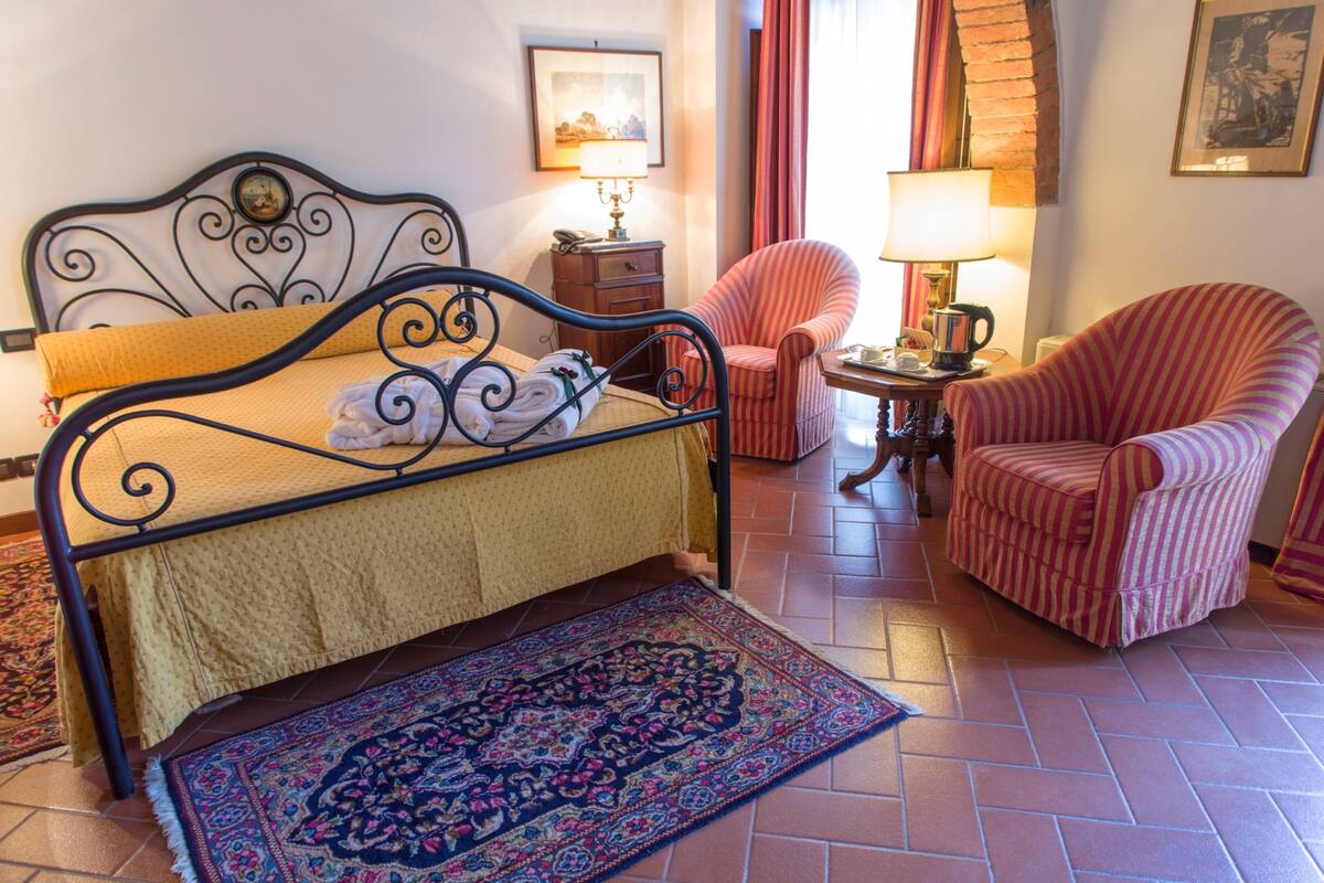 A neatly arranged bedroom with a bed, two chairs, a nightstand, and a rug.