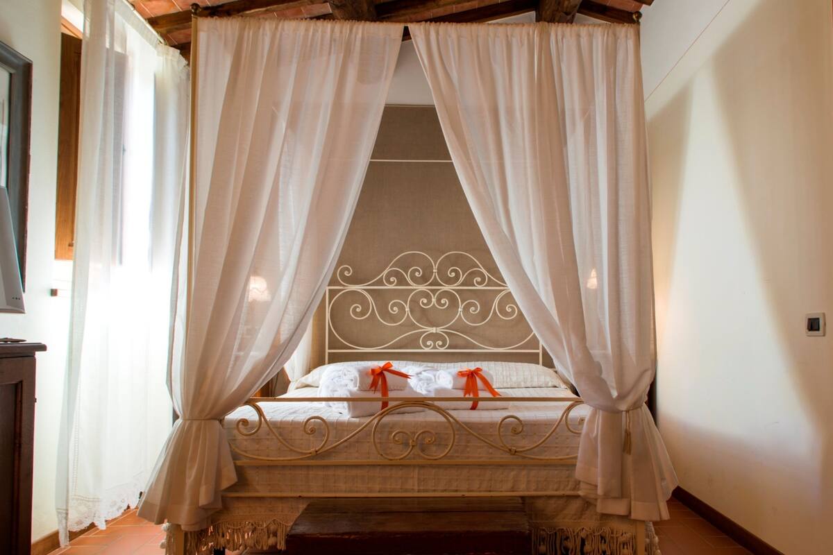 A four-poster canopy bed with white linens and a red ribbon, a wooden headboard, and a red carpeted floor.