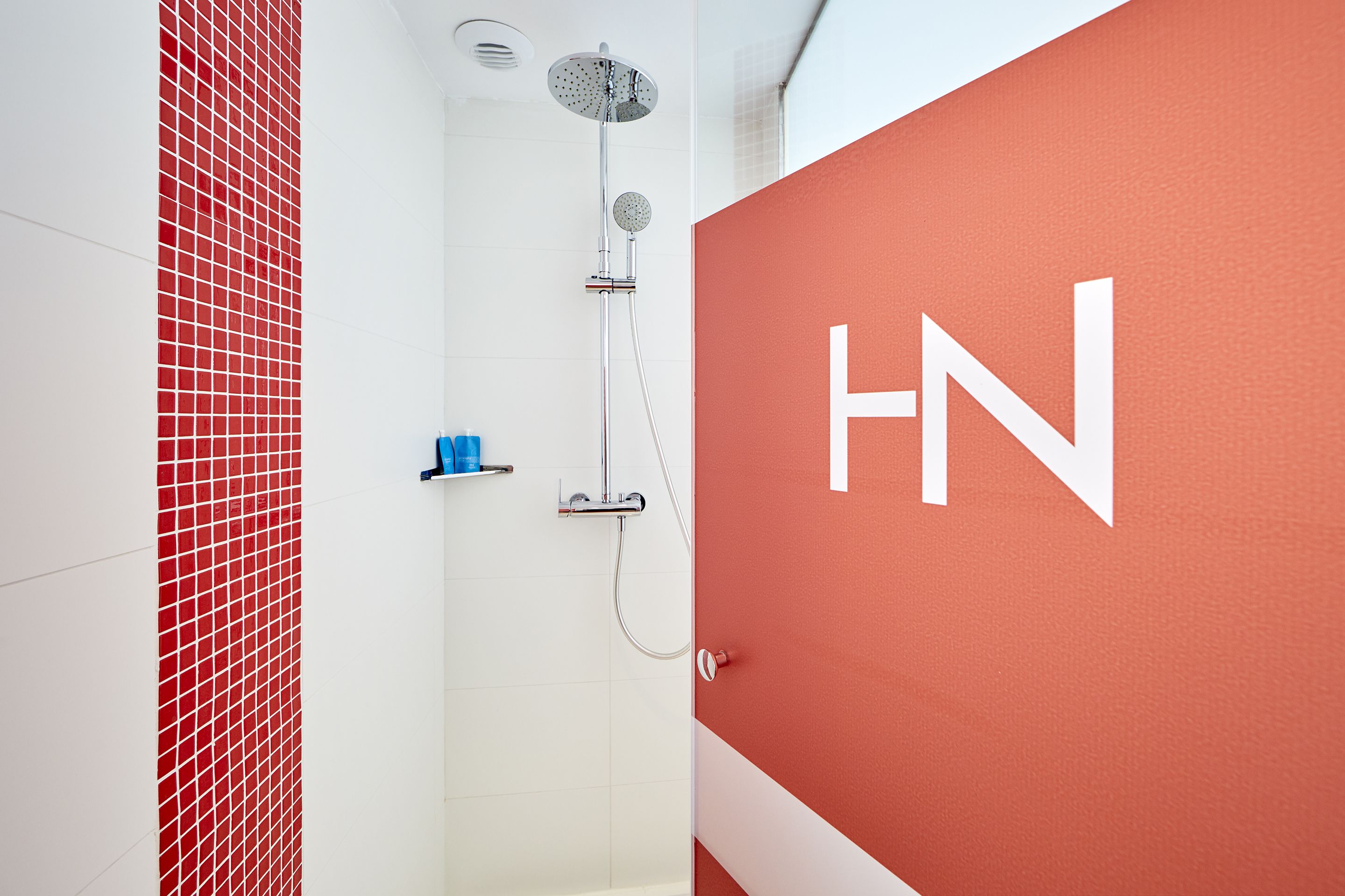 A modern bathroom with a red accent wall, a shower with a rain showerhead, and a visible water heater.