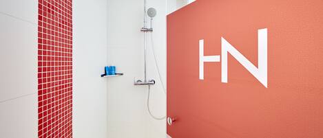 A modern bathroom with a red accent wall, a shower with a rain showerhead, and a visible water heater.