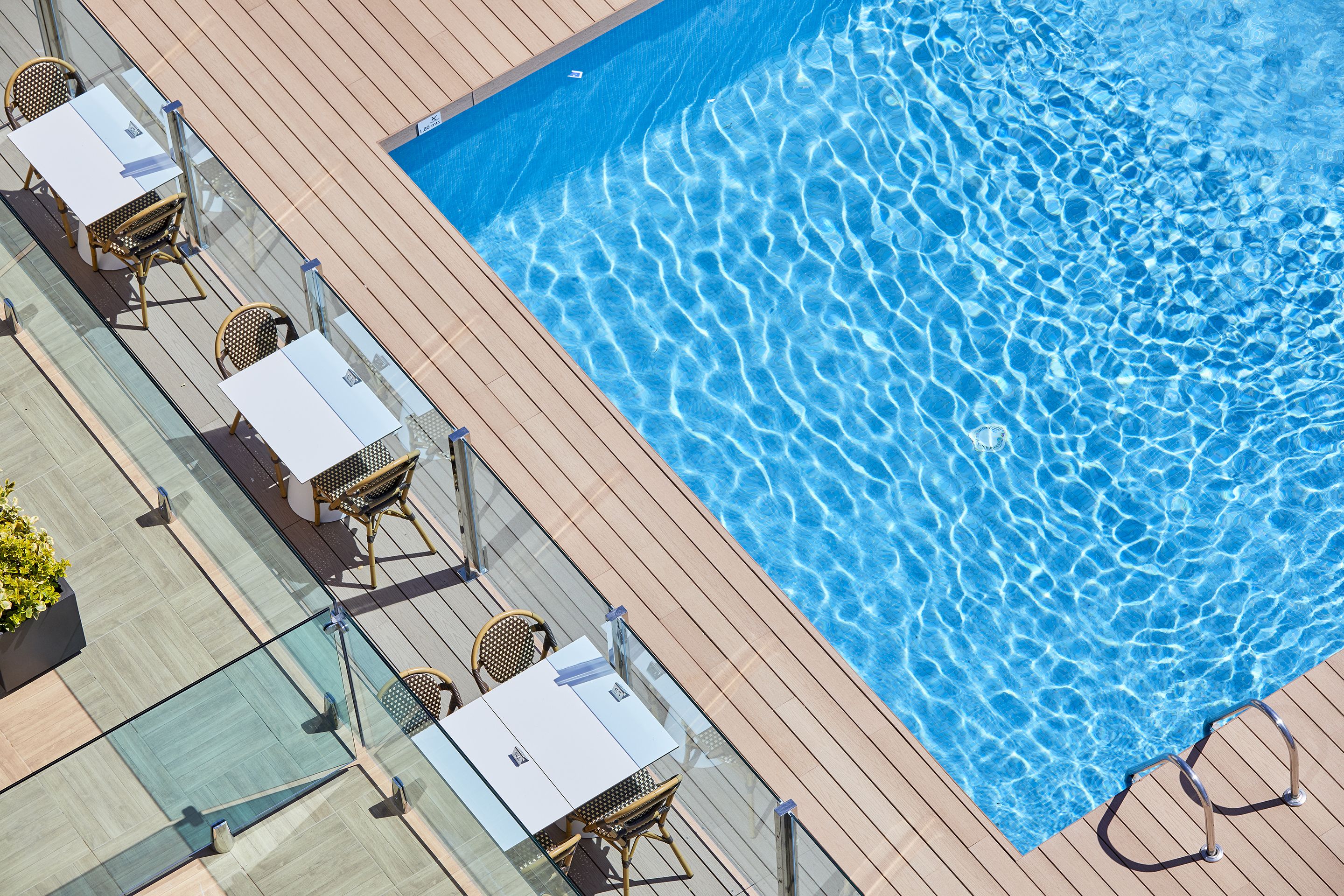 A poolside area with a glass barrier, lounge chairs, and a wooden deck.