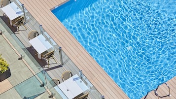 Zona junto a la piscina con barandilla de cristal, sillas de descanso y una terraza de madera.