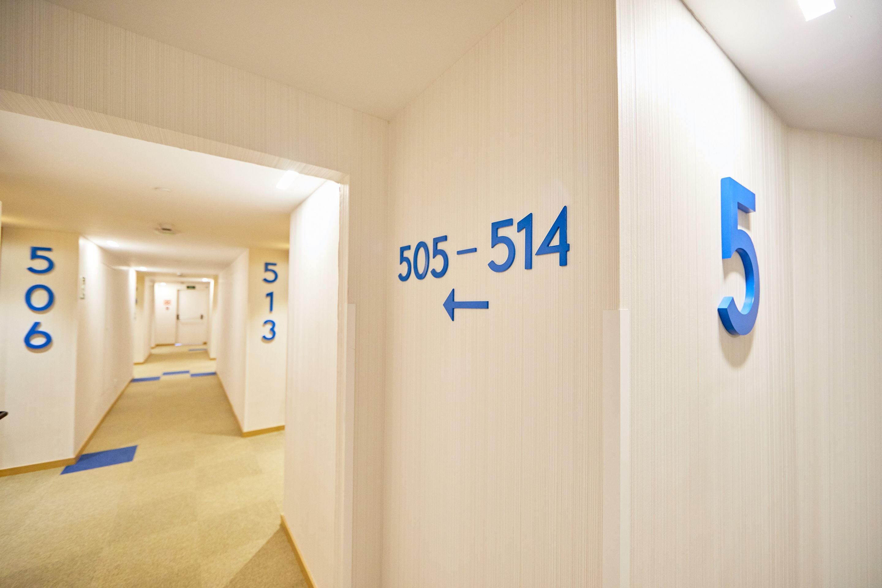 Een hotelgangen met genummerde deuren, een tapijtvloer en een pijlpijl op de muur.