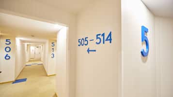 Een hotelgangen met genummerde deuren, een tapijtvloer en een pijlpijl op de muur.