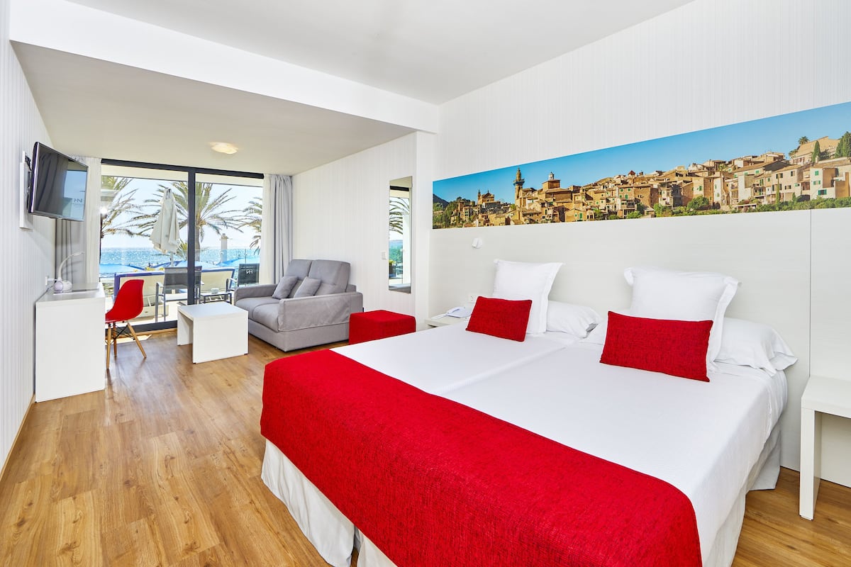 Una habitación de hotel moderna con una cama grande, un sofá, una mesita y un televisor.
