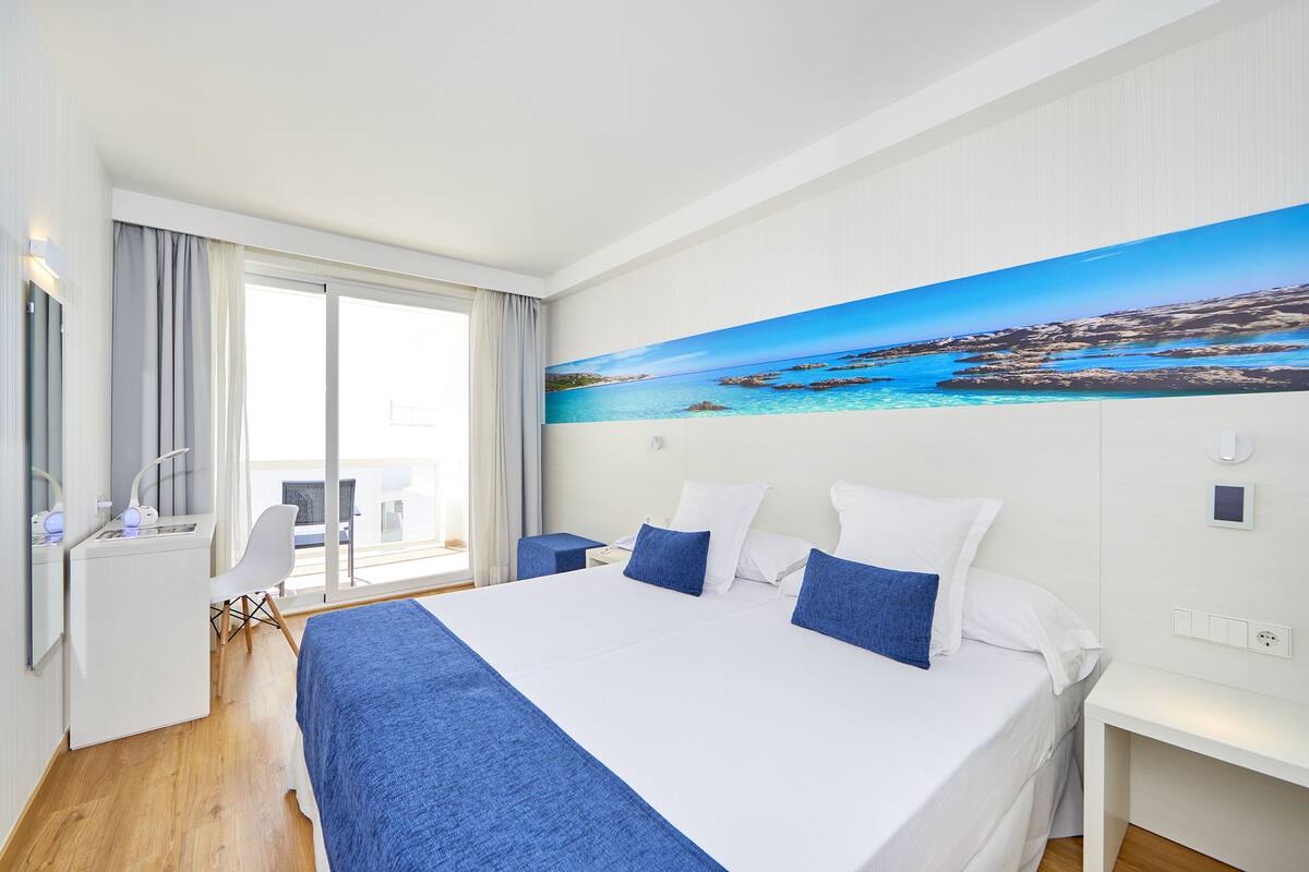 Habitación de hotel con una cama grande, un escritorio y una silla. En la pared, un cuadro con una escena costera.