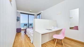 Une chambre d’hôtel moderne équipée d’un lit, d’un bureau, d’une chaise et d’une grande fenêtre donnant sur l’océan.