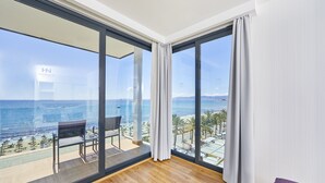 Moderni hotellihuone, jossa on suuri lasi-ikkuna, puulattia ja näkymä rannalle ja merelle.