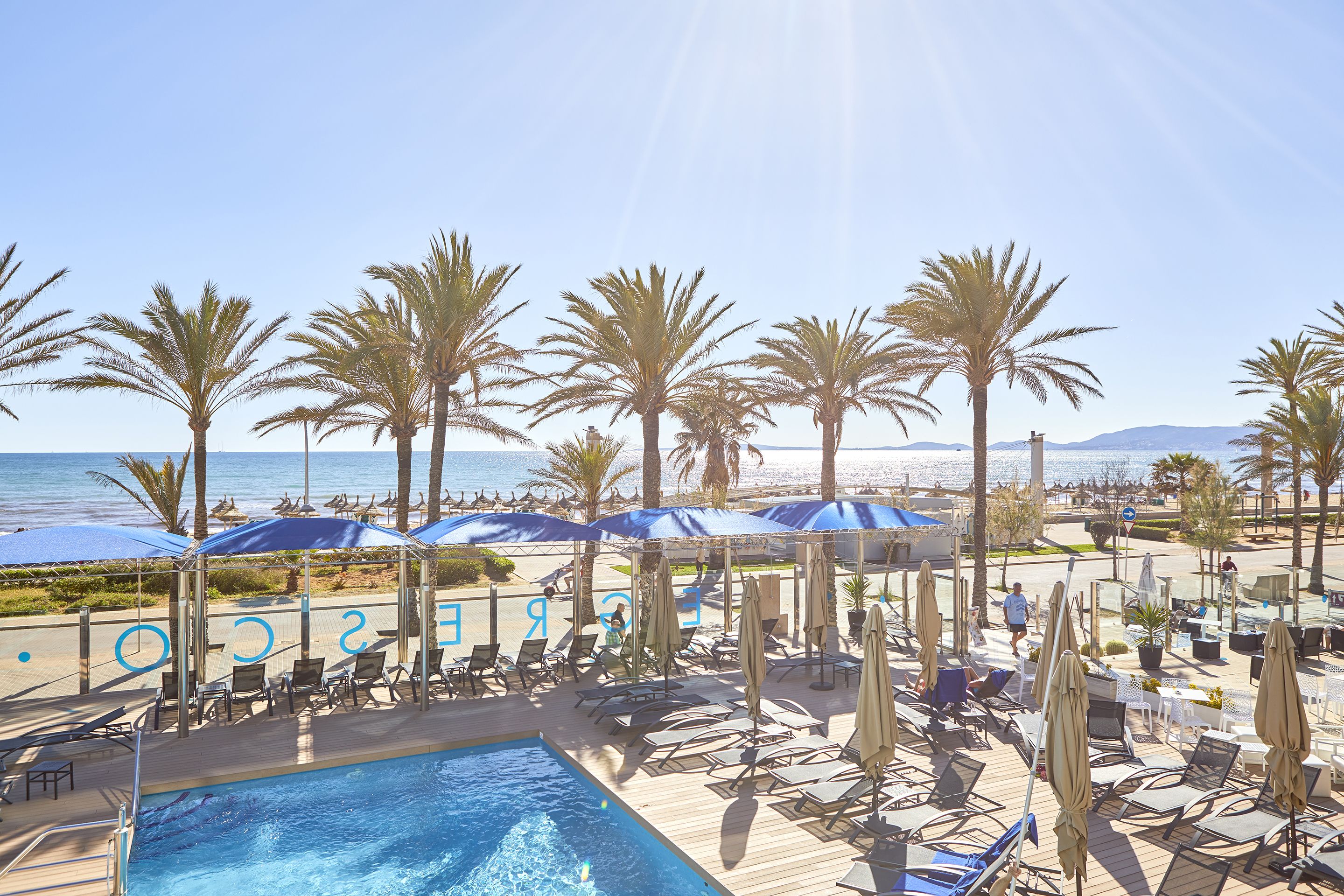 Un espace aménagé au bord de la piscine, avec des chaises longues et des parasols, offrant une vue sur la plage et l’océan.