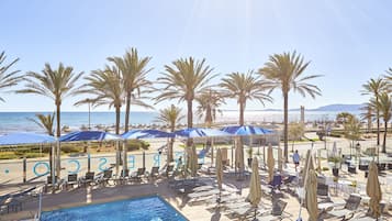 Un espace aménagé au bord de la piscine, avec des chaises longues et des parasols, offrant une vue sur la plage et l’océan.