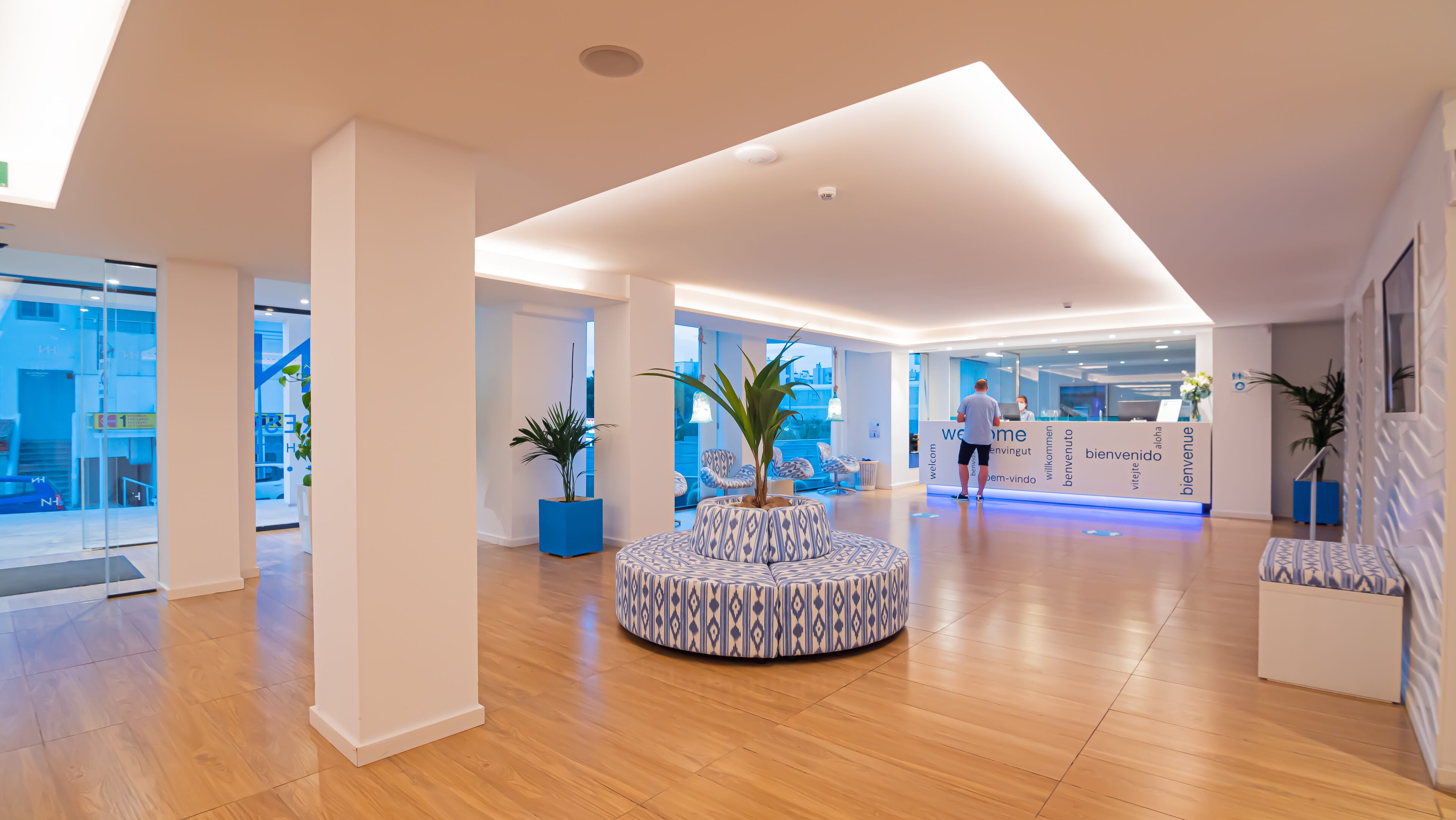 Een moderne hotellobby met een receptiebalie, een zithoek en grote ramen.
