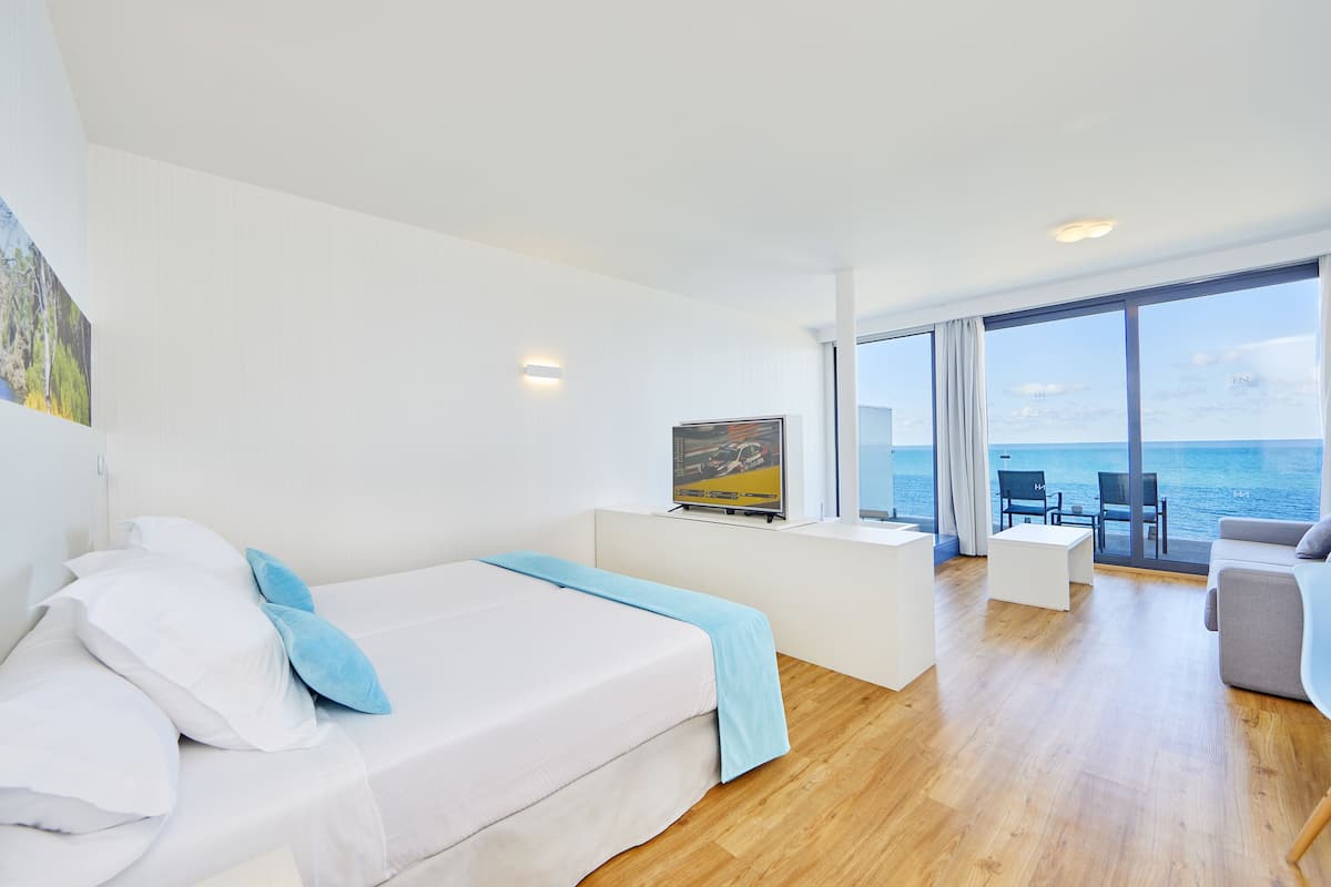 Habitación de hotel moderna con cama, televisión, zona de estar con vistas al mar y balcón.
