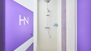 Un baño con ducha, pared de azulejos blancos y una pared de acento púrpura con las letras "HN".