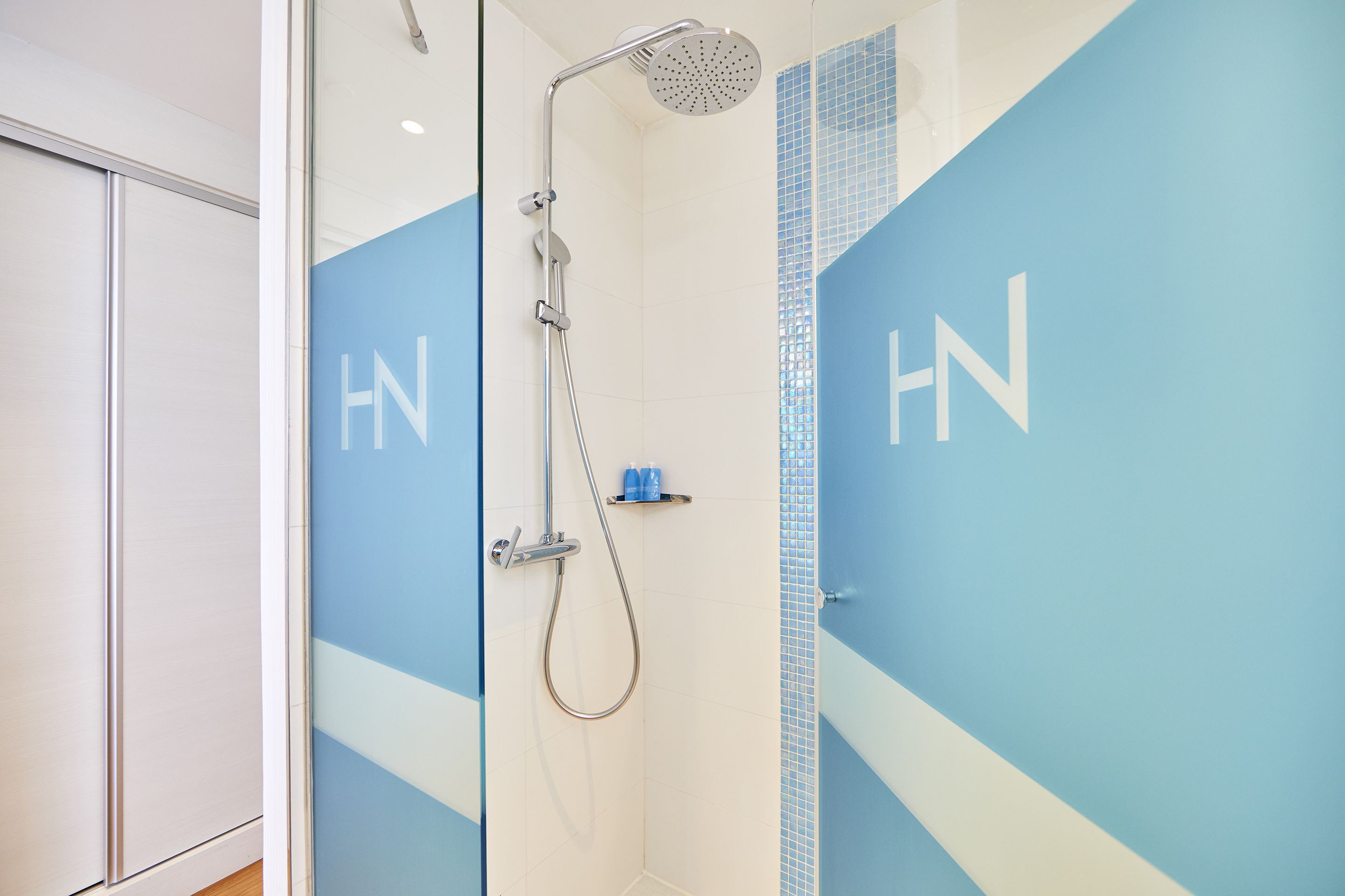 Un baño moderno con ducha, pared de acento azul y las letras 'HN' en la pared.