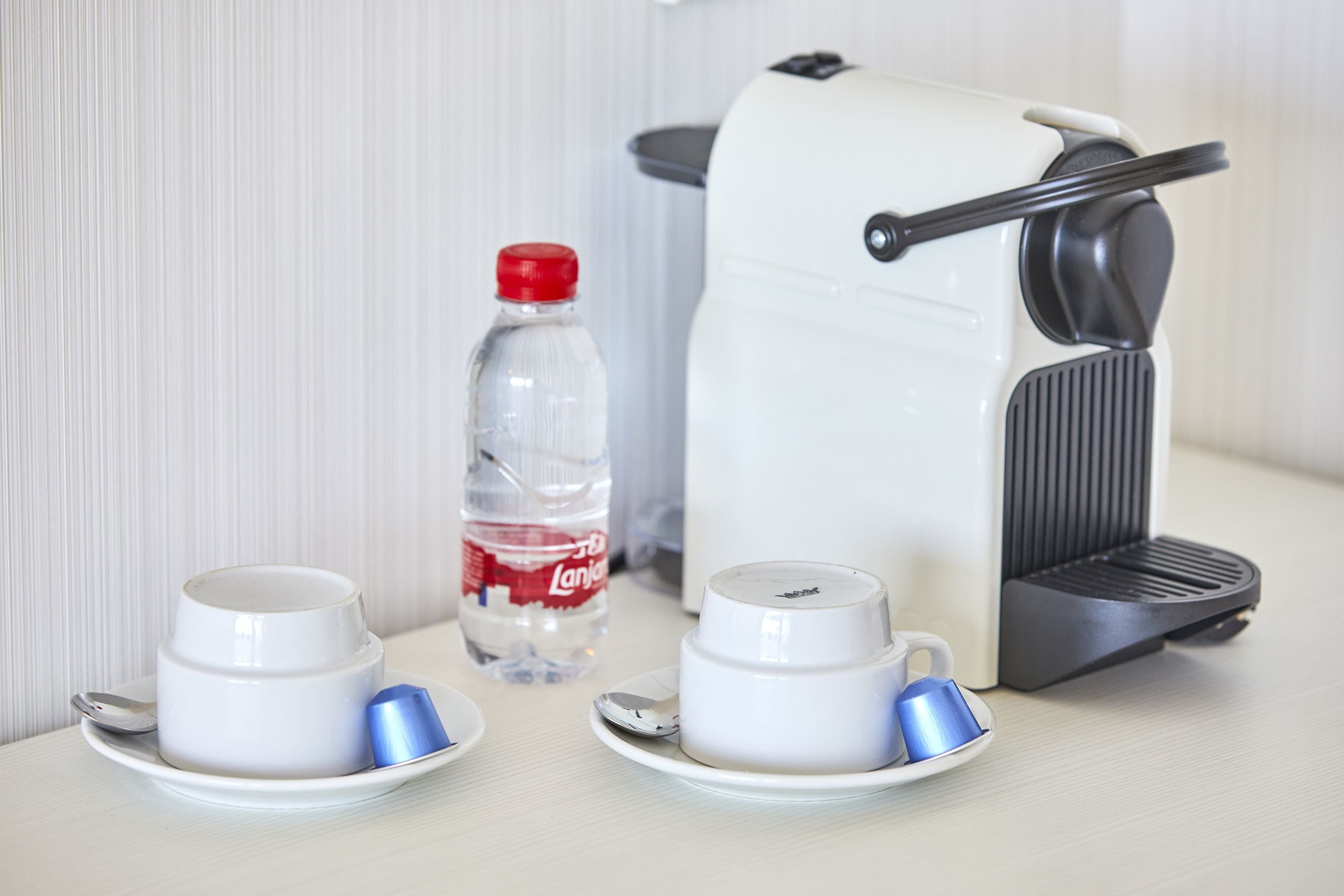 A coffee maker, two cups, a spoon, and a water bottle on a table.