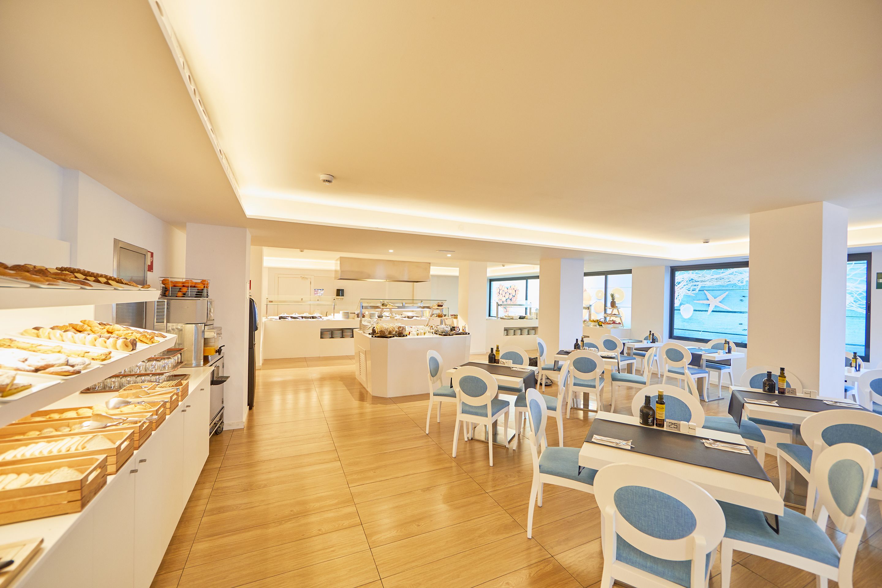 Un espace repas moderne avec un plancher en bois, des chaises blanches et bleues, et un buffet proposant divers plats.