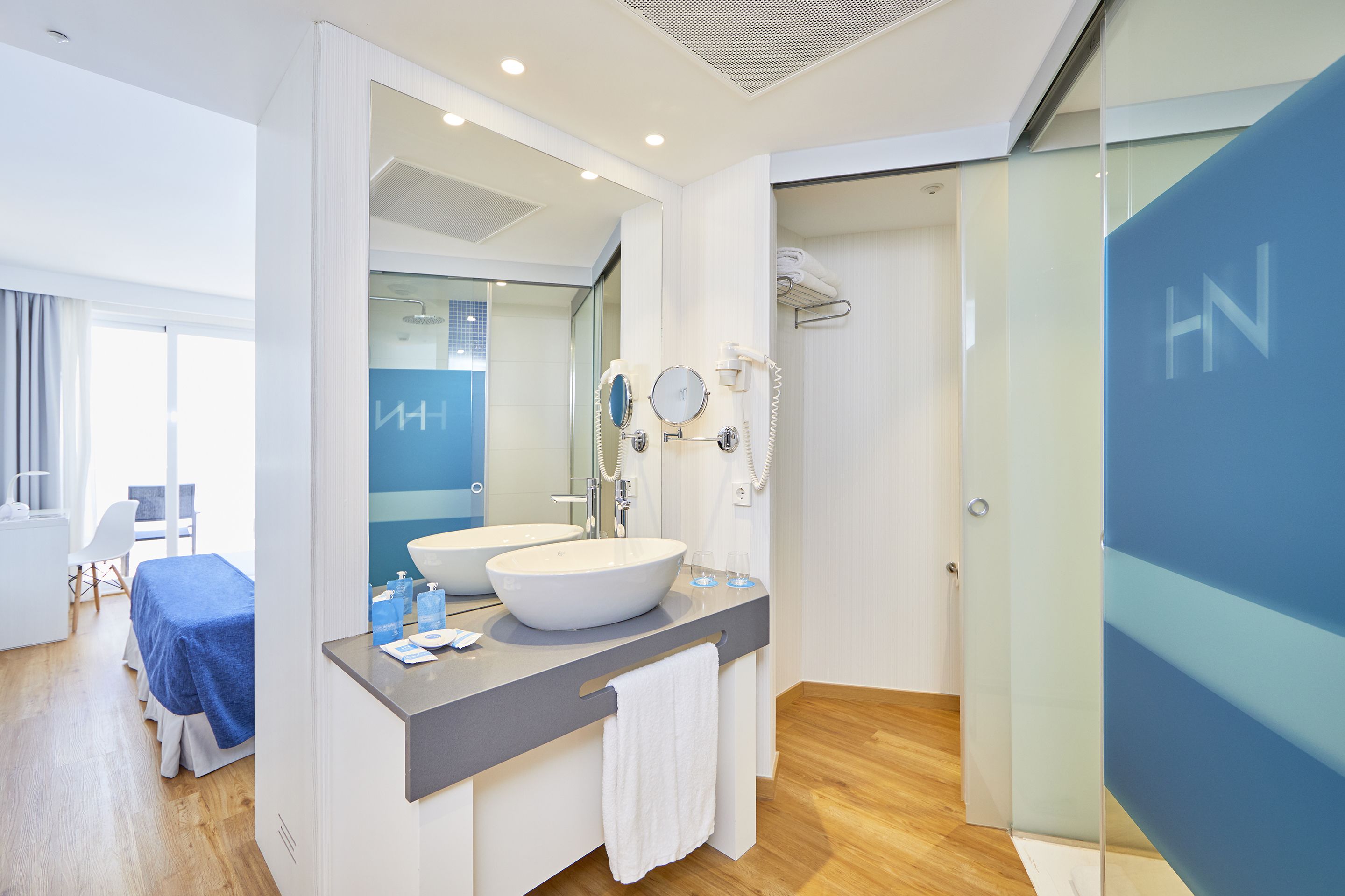 A modern bathroom with two sinks, a large mirror, and a glass shower enclosure.